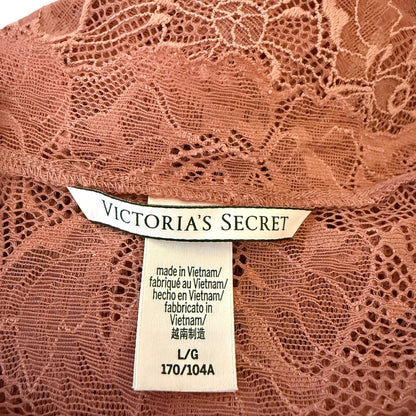 Close-up of a Victoria's Secret garment label sewn onto dusty rose pink lace fabric, showing the brand name and size information.