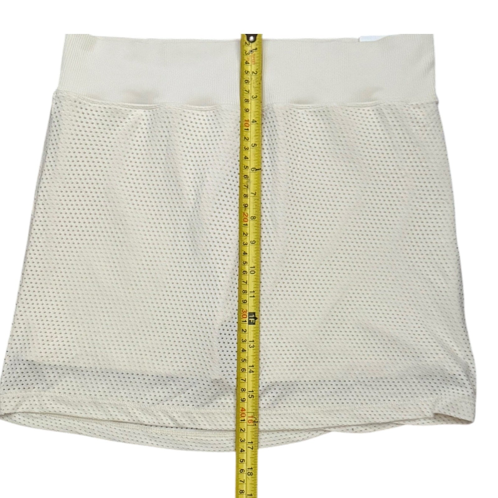 Mesh skort shown flat on a white background with a yellow measuring tape running vertically down the center to indicate size.