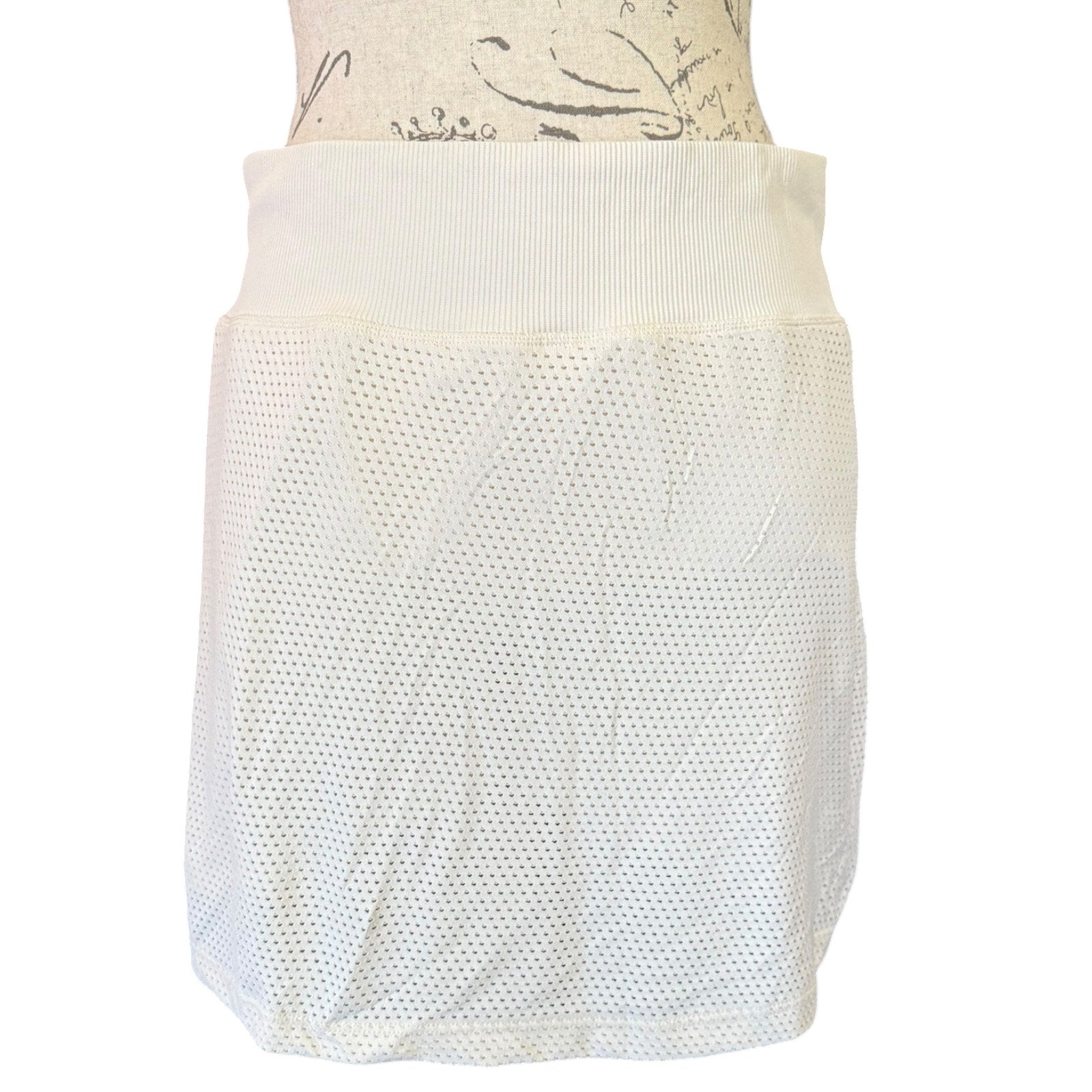 An mesh skort with a wide ribbed waistband, displayed on a mannequin torso against a plain white background.