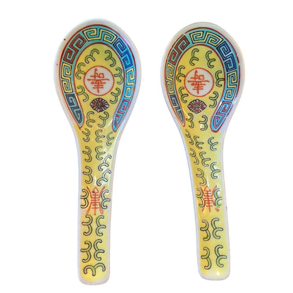 Two decorative Chinese spoons with a yellow and white glaze, featuring traditional Chinese patterns in blue, green, red, and gold.