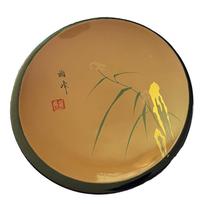 A round wood plate with a glossy warm brown-gold glaze, decorated with green bamboo leaves, a yellow lotus flower, black calligraphy, and a red seal on a white background.