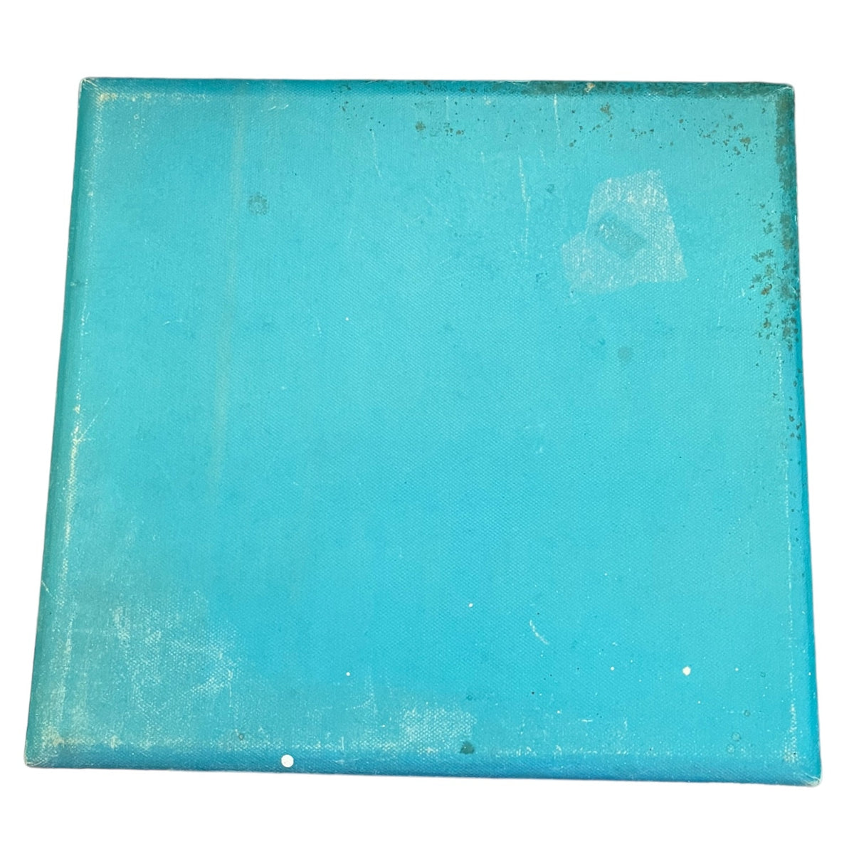 A square turquoise blue box with a distressed, weathered finish showing signs of wear, scratches, and a small piece of residue on the surface, isolated on a white background.