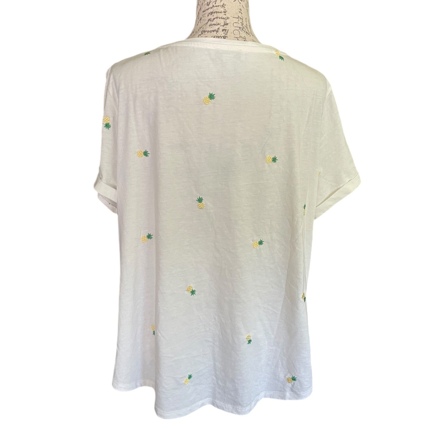 An white short-sleeve t-shirt with small embroidered yellow and green pineapple motifs, displayed on a mannequin torso against a white background.