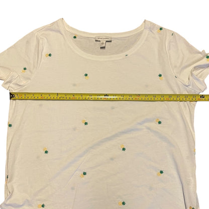 An white short-sleeve t-shirt with a small pineapple print, shown with a yellow tape measure across the chest to indicate size.