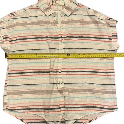 A striped short-sleeve button-up shirt laid flat on a white background, with a yellow tape measure stretched horizontally across the chest to show the width. The shirt features horizontal stripes in beige, brown, light blue, and coral red on an off-white base.