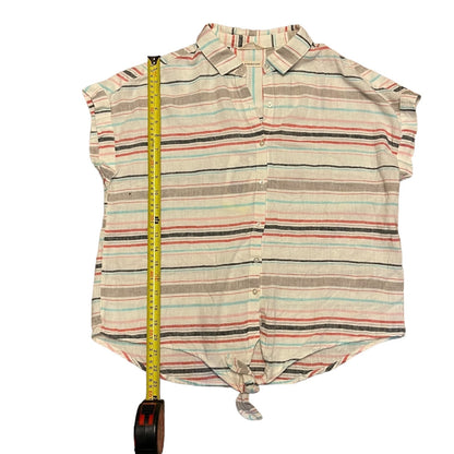 A short-sleeve collared button-up shirt with horizontal stripes in beige, brown, light blue, and coral, laid flat on a white background with a yellow tape measure standing vertically to show its height.