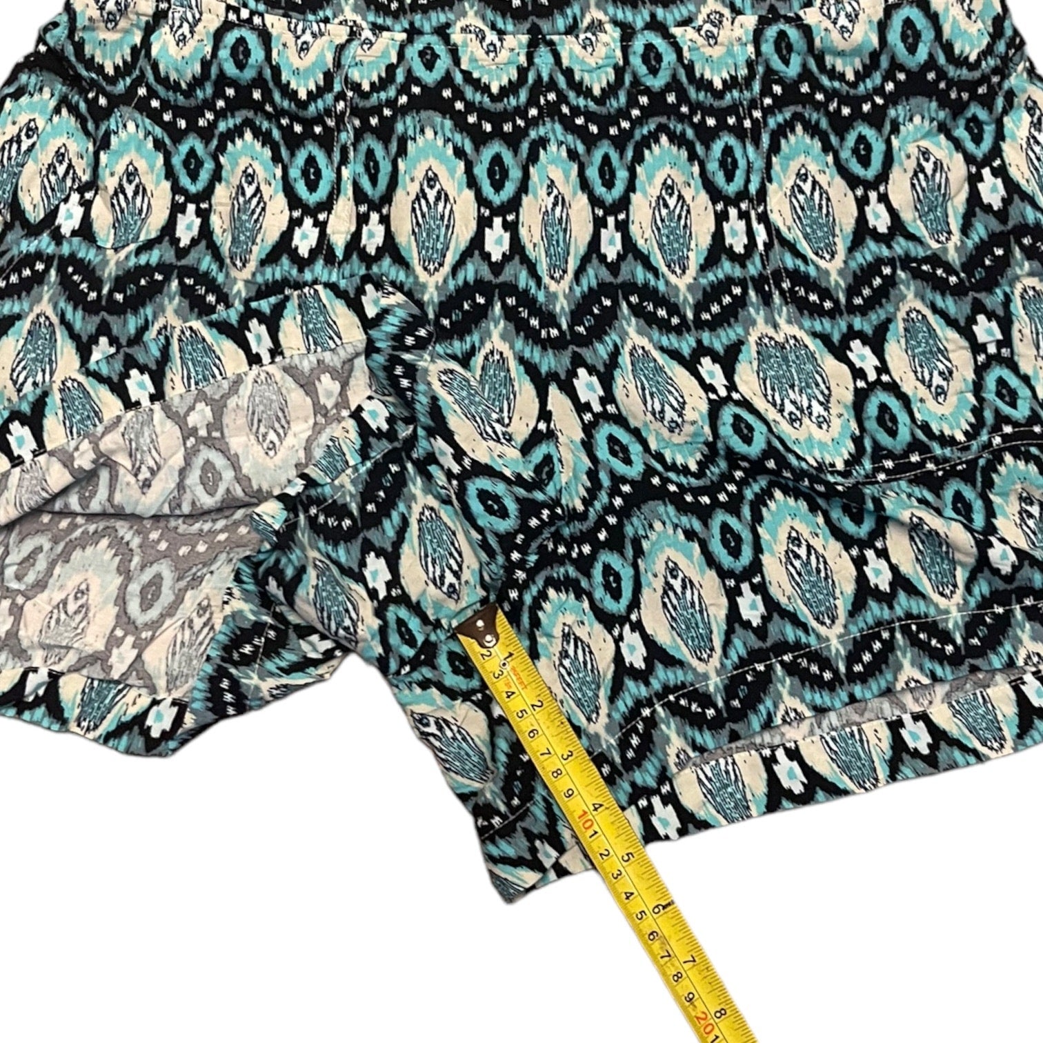 A close-up of patterned shorts  shown with a yellow measuring tape to indicate inseam against a white background.