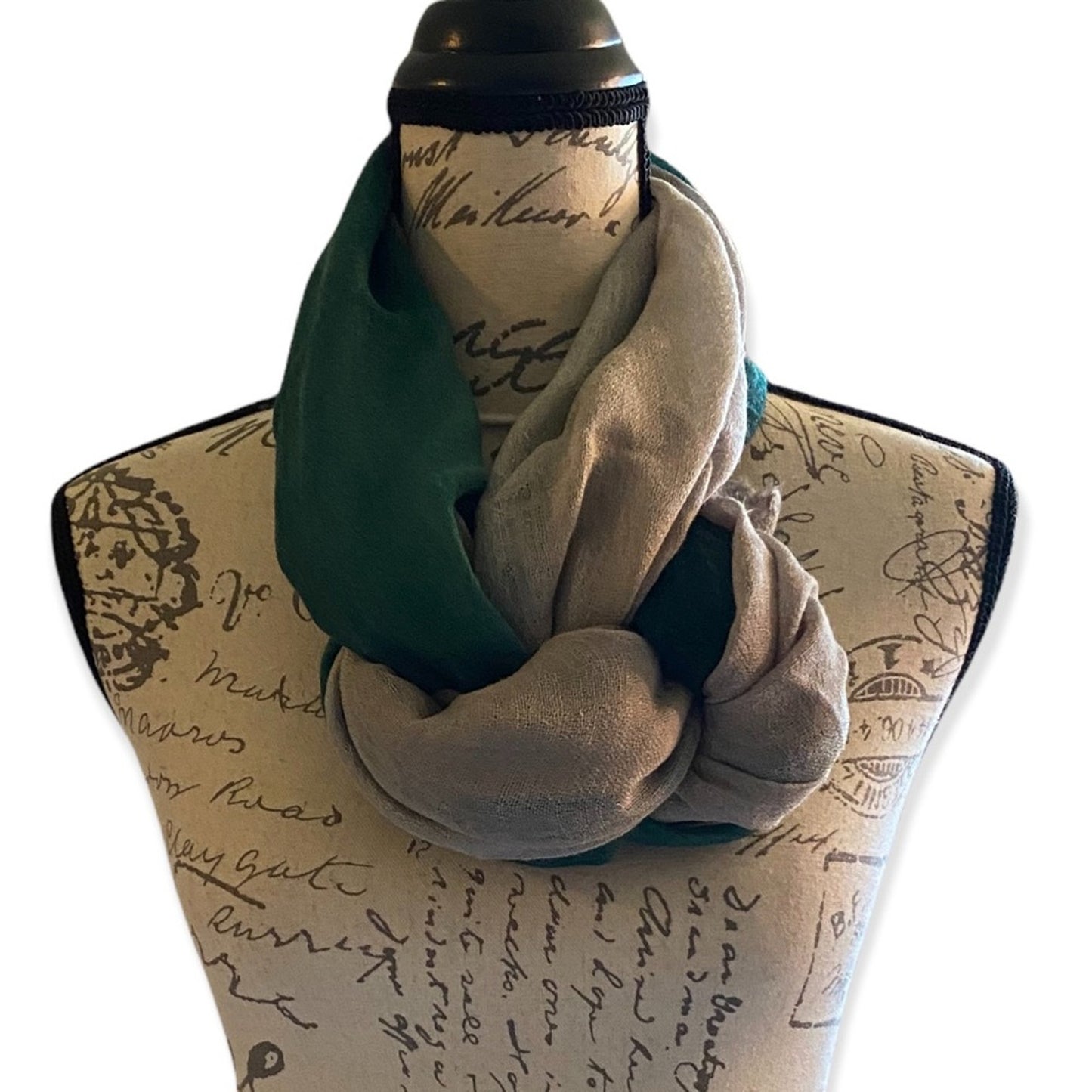 A two-tone scarf in dark green and light taupe, styled on a decorative dress form mannequin against a plain white background.