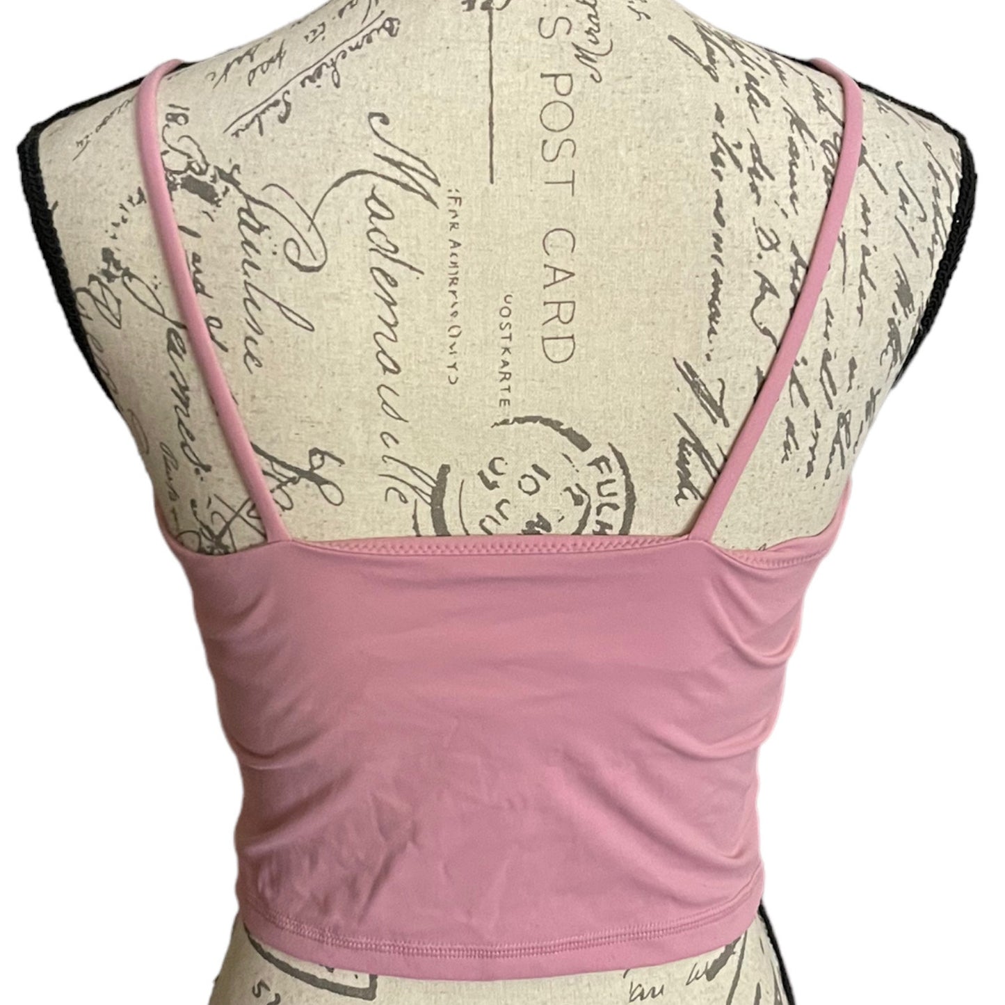 A pink spaghetti-strap crop top SPORTS bra displayed on a vintage-style paper dress form mannequin against a white background.