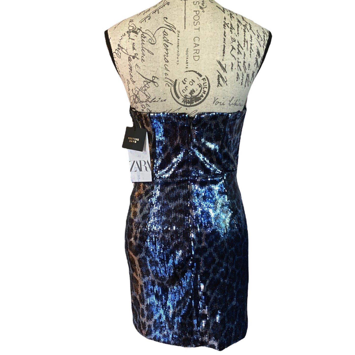 A strapless sequined mini dress displayed on a vintage-style paper mannequin torso. The dress features a blue and black sequined leopard print pattern on the lower half, transitioning to a solid shimmering blue upper section.