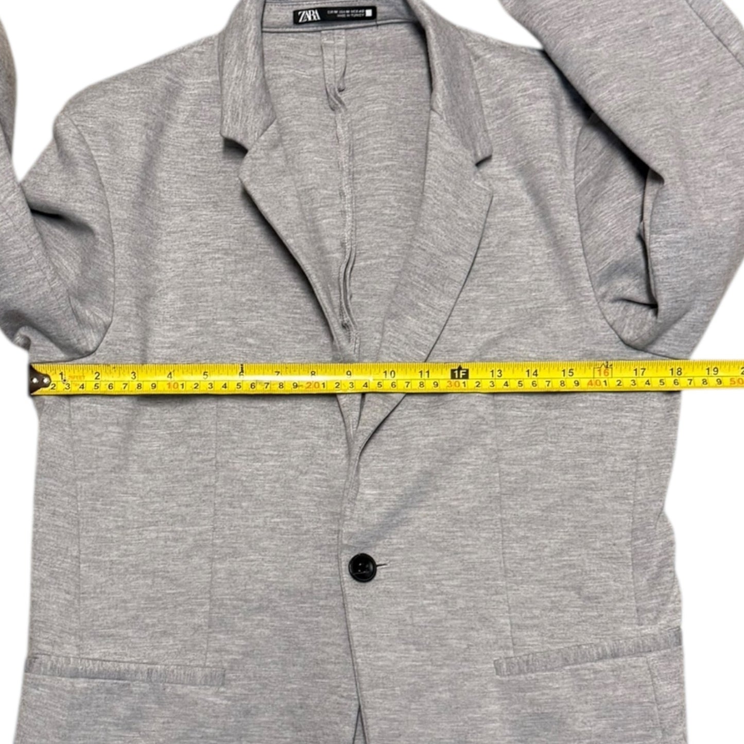 Gray blazer with a measuring tape draped over it on a white background
